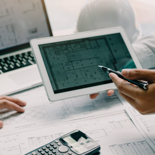 Two engineering working together and using digital tablet looking blueprint and analysis with architectural plan on desk.